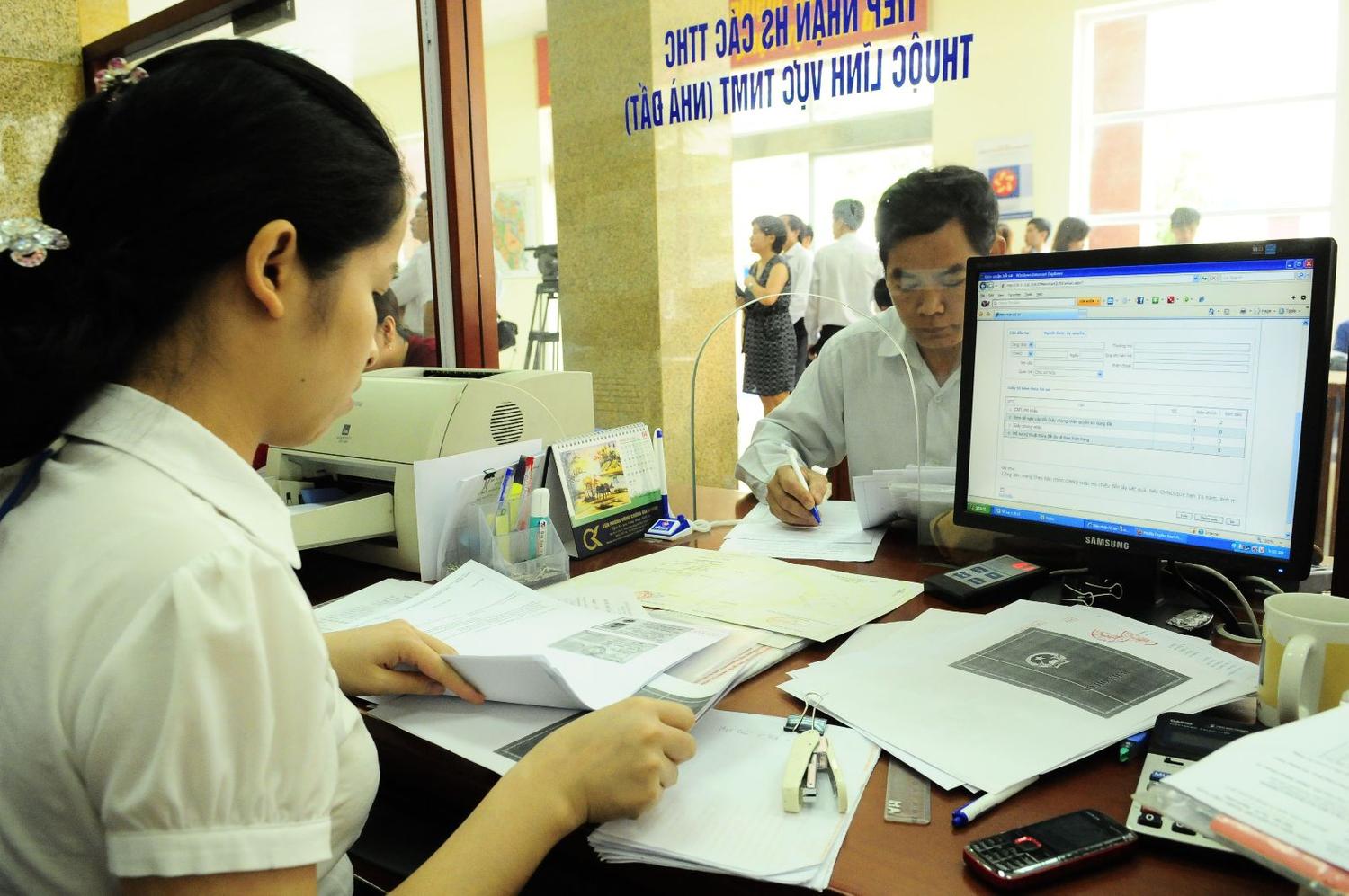 2 người đang trao đổi với nhau, trên tay họ cầm nhiều giấy tờ