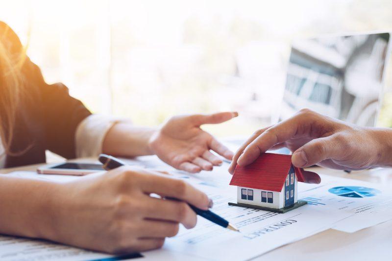 hai bàn tay đang chỉ vào tờ hợp đồng mua bán, bên cạnh là mô hình ngôi nhà