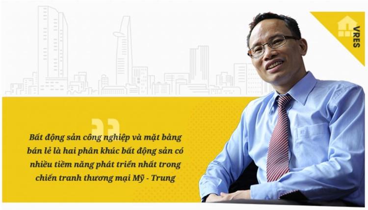 Một người đeo kính đang ngồi, nhìn ống kính, cười tươi