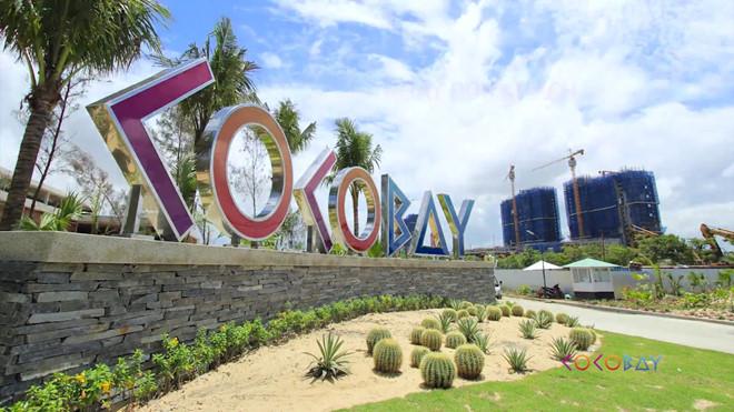 biển tên dự án Cocobay Đà Nẵng có cây xanh và dự án đang xây dựng phía xa