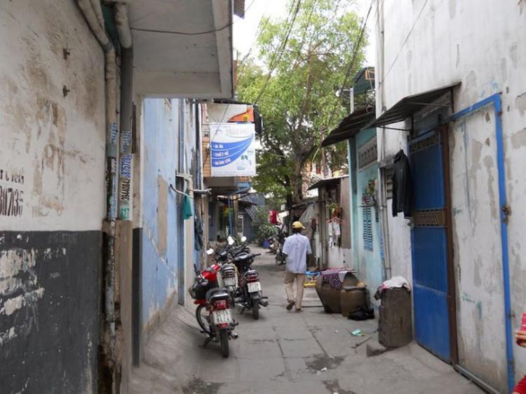 Ngõ hẻm ở giữa, hai bên là các dãy nhà san sát, nhiều xe máy dựng trên ngõ, người đi lại.