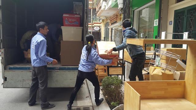 Ô tô tải trong ngõ hẻm, một số người đang khuân đồ từ xe vào nhà.