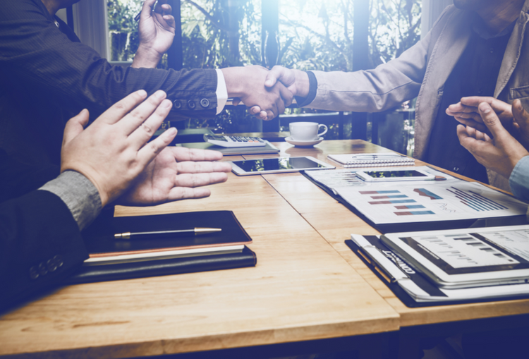 Trên bàn làm việc có nhiều sổ sách, hai người bắt tay nhau, hai người vỗ tay.