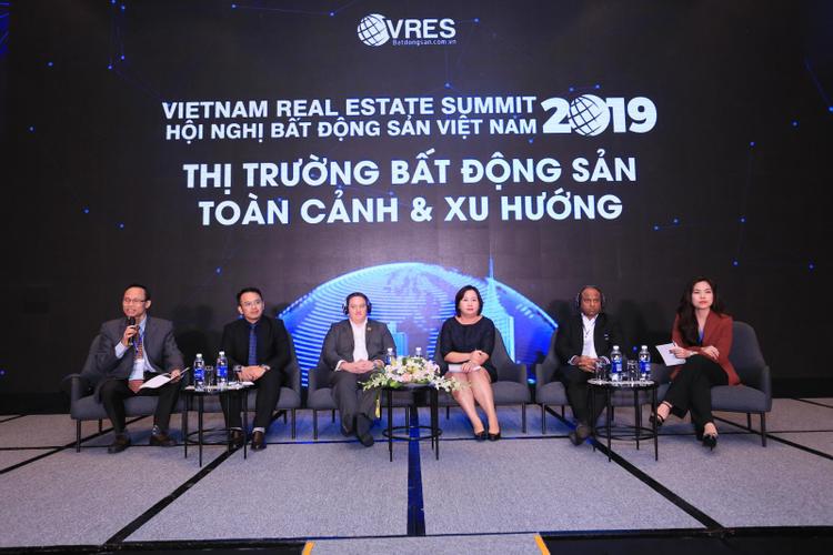 Khu vực sân khấu có phông nền tối, các dòng chữ màu trắng sáng, bên dưới là một dãy người ngồi trên ghế.