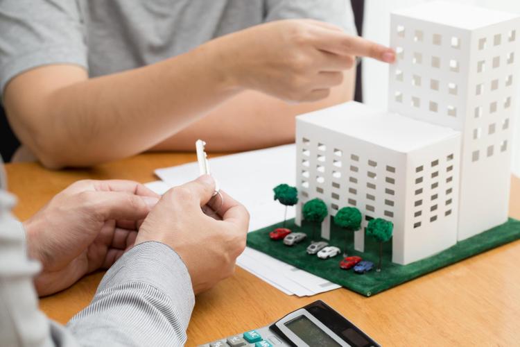 một bàn tay cầm chiếc chìa khóa, một bàn tay chỉ vào mô hình khu chung cư