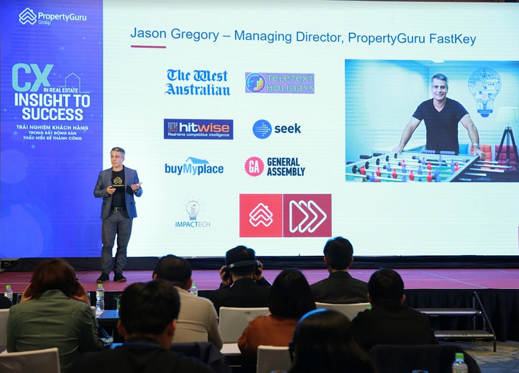 một người đàn ông đứng thuyết trình trên khán đài, phía dưới là máy chiếu 