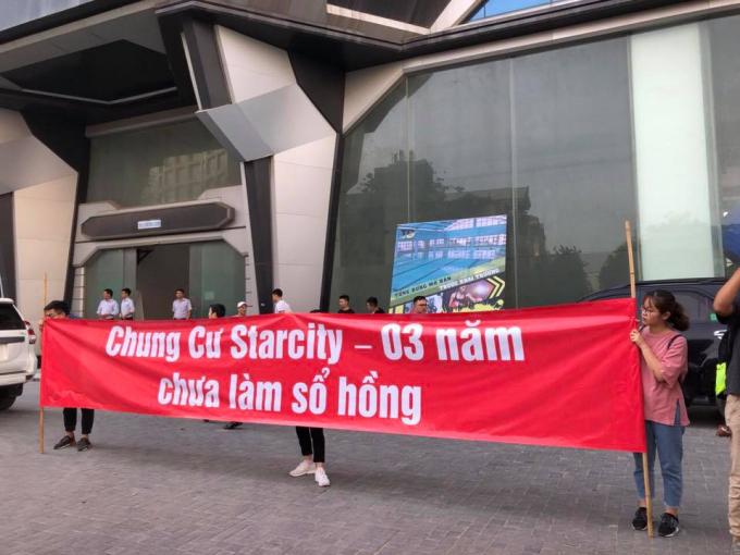 nhiều người cầm băng rôn đỏ đứng trước một khu chung cư