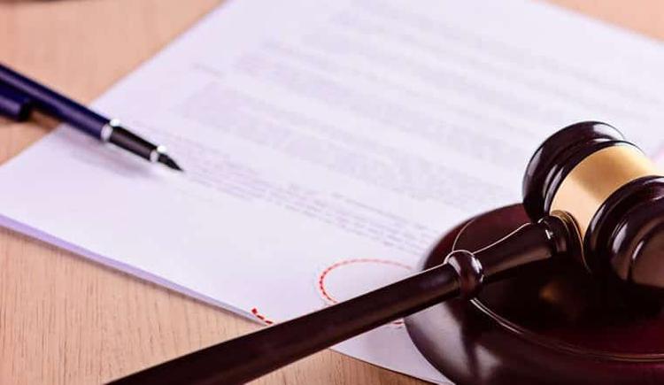 một cái bút, một tờ giấy và biểu tượng chiếc búa của ngành luật đặt trên bàn
