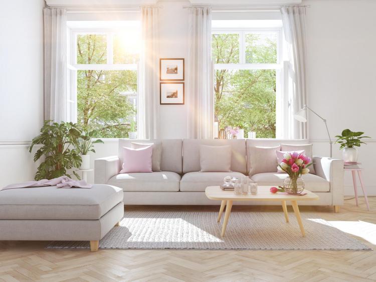 Phòng khách màu trắng với sofa trắng, lọ hoa trên bàn... đặt cạnh cửa sổ nhiều ánh nắng.