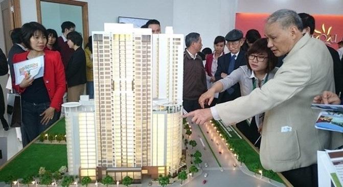 Nhiều người quây quanh sa bàn một dự án bất động sản là tòa chung cư cao tầng màu trắng