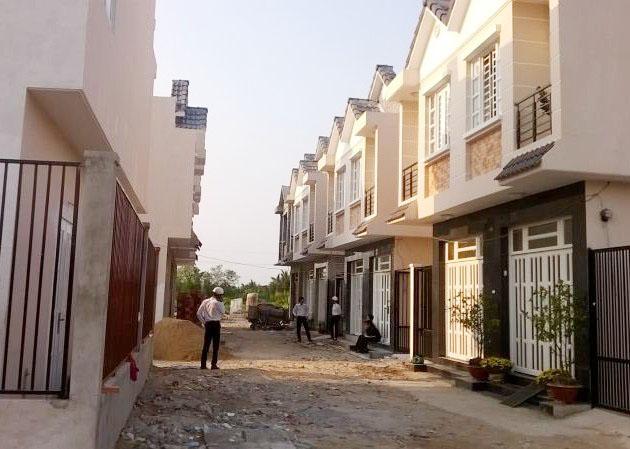 Hai dãy nhà xây sẵn nằm đối diện nhau, ở giữa lối đi có người đứng nghe điện thoại