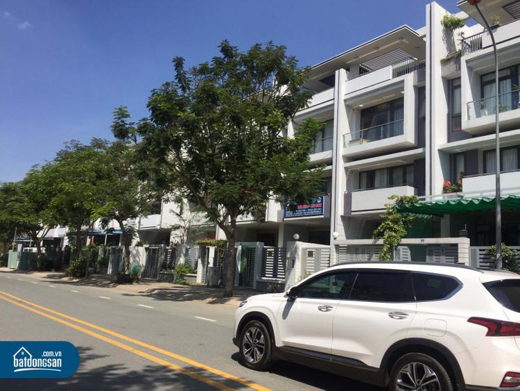 Dãy nhà liền kề nằm cạnh con đường lớn, cây xanh, ô tô màu trắng.