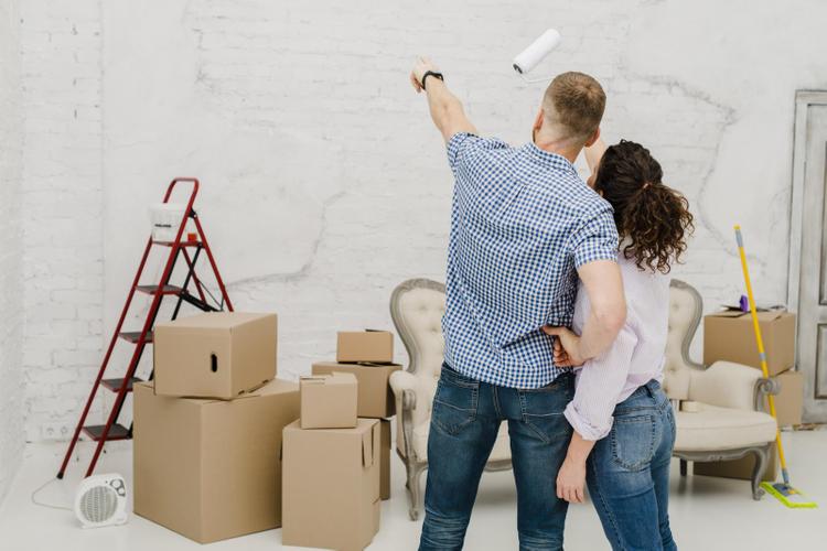 1 người đàn ông và 1 người phụ nữ đang chỉ vào bức tường của căn phòng, xung quanh là dụng cụ sửa chữa nhà