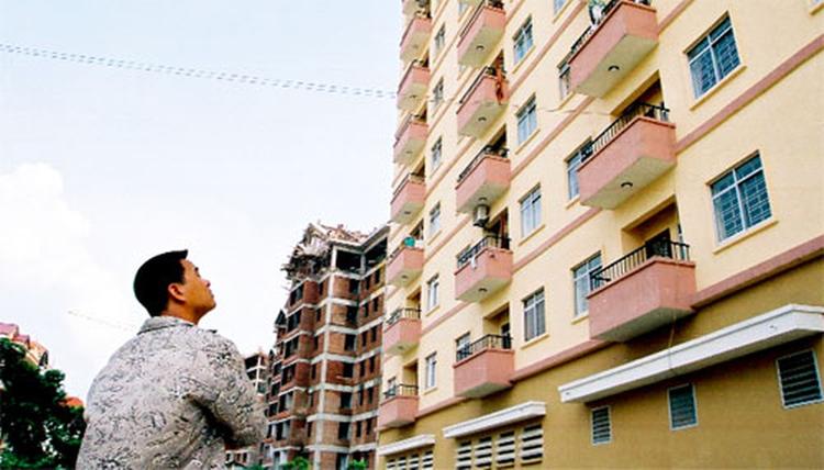 1 người đàn ông ngước lên nhìn 1 tòa nhà chung cư đã cũ