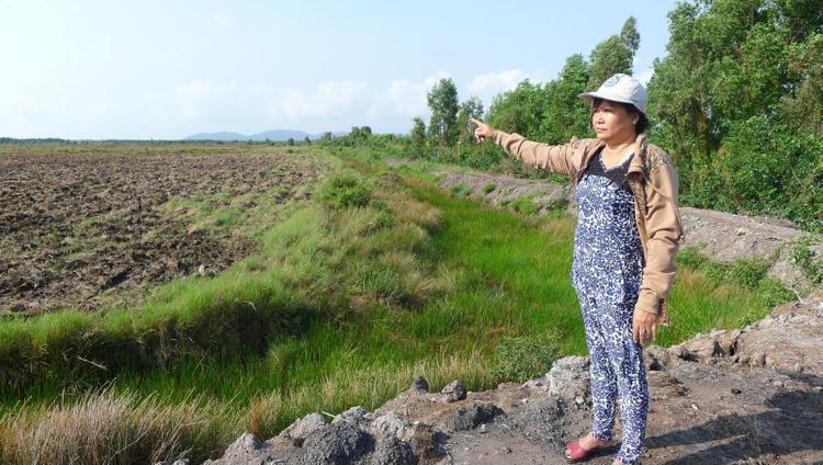 một người phụ nữ đứng chỉ tay ra khu đất trống