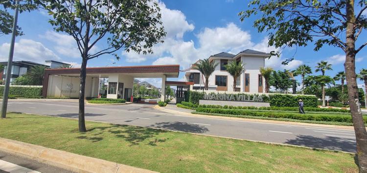 Bên ngoài cổng vào một dự án bất động sản tại tỉnh giáp ranh Tp.HCM, đường lớn vắng vẻ, nhiều cây xanh.