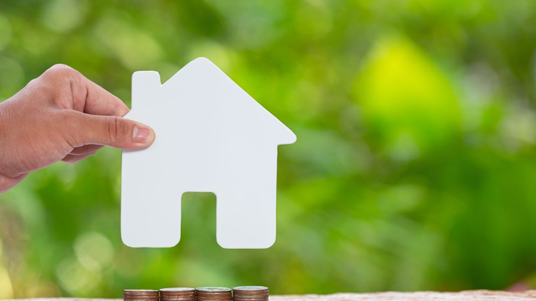 Close-up picture of a pile of coins and a hand holding a model house