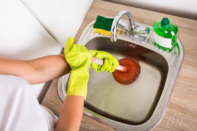 Close-up Of Person Using Plunger In The Kitchen Sink