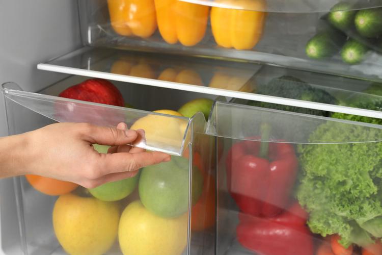 Woman opening refrigerator drawer with fresh fruits
