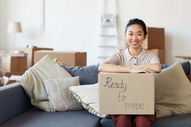portrait of young Asian woman holding cardboard box with ready to move inscription and smiling looking at camera, copy space