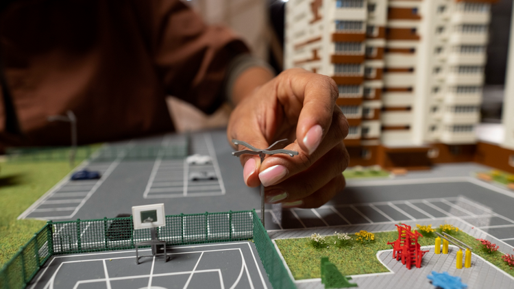 A person's hand places a small light post onto a detailed architectural model
