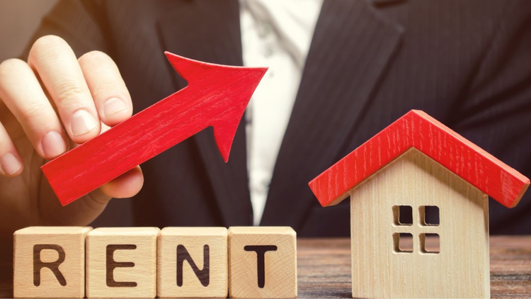 A hand placing a red arrow above wooden blocks spelling "RENT" and a model house, symbolising rent yield and growth.