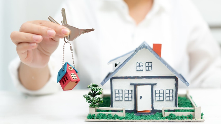 A person holding a bunch of keys with a model house charm, and a model house is placed on the table.