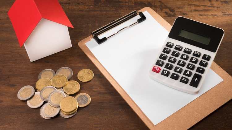 A model house, coins, and a calculator on a clipboard, representing property taxes and financial calculations.