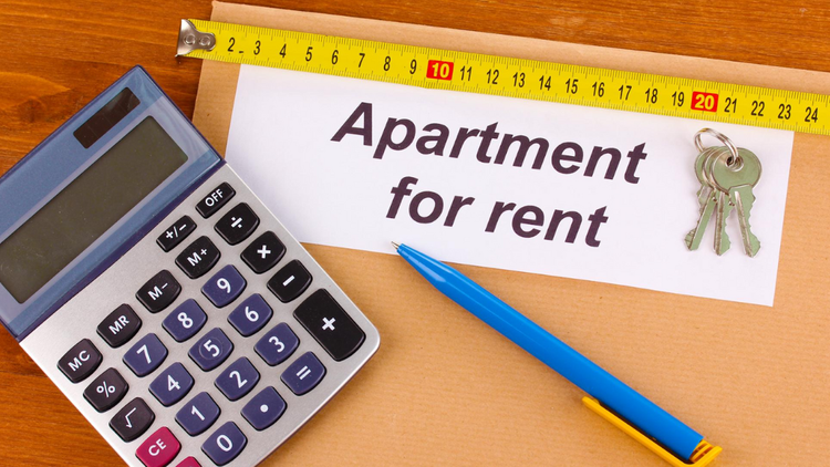 A calculator, a blue pen, a measuring tape, and a set of keys rest on a brown envelope