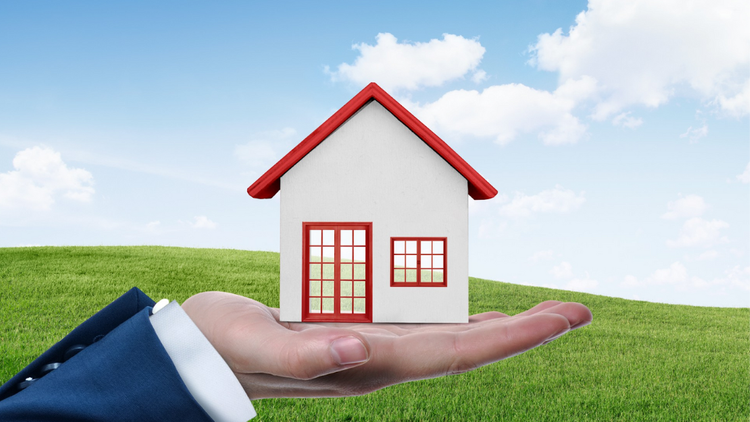 A person holding up a miniature white house with a red roof