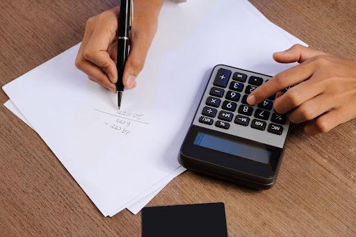 Close-up of a person calculating on a calculator and writing.