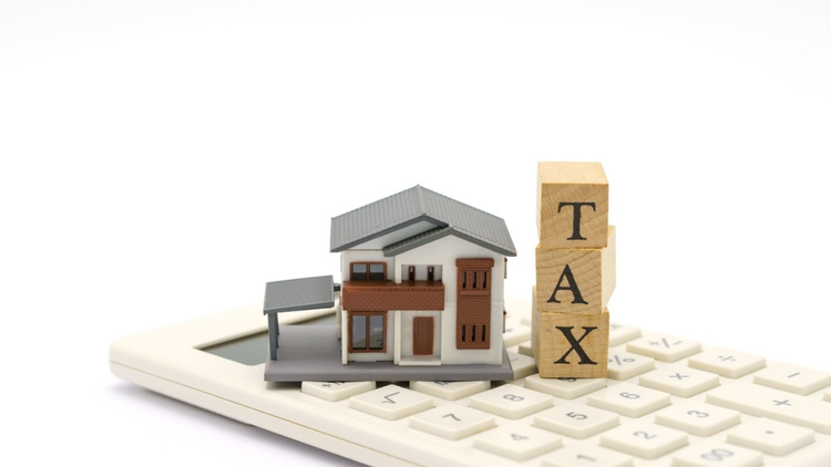 A model and wooden blocks spelling “TAX” are placed on a white calculator