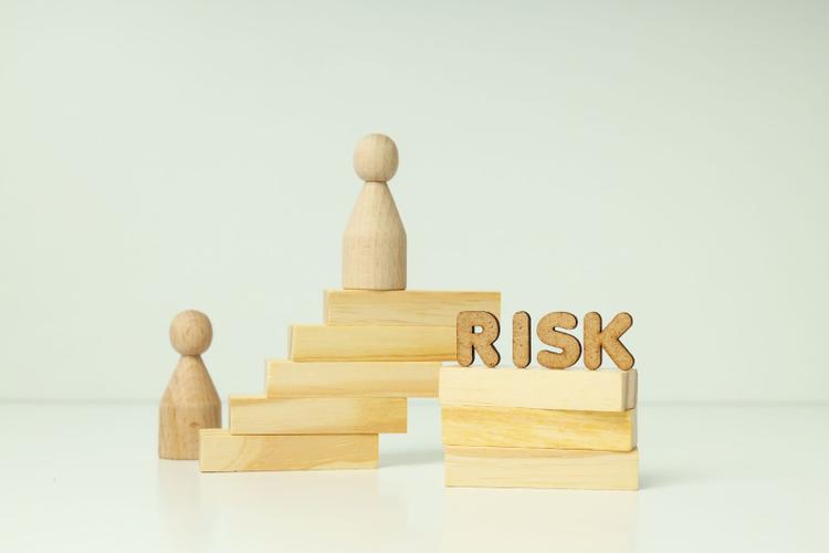Stack of wooden blocks, two wooden human models and a wooden-carved block spelling “RISK”.
