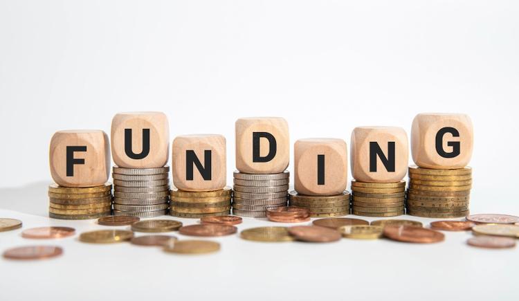 Wooden dice spelling “FUNDING” are placed on piles of coins