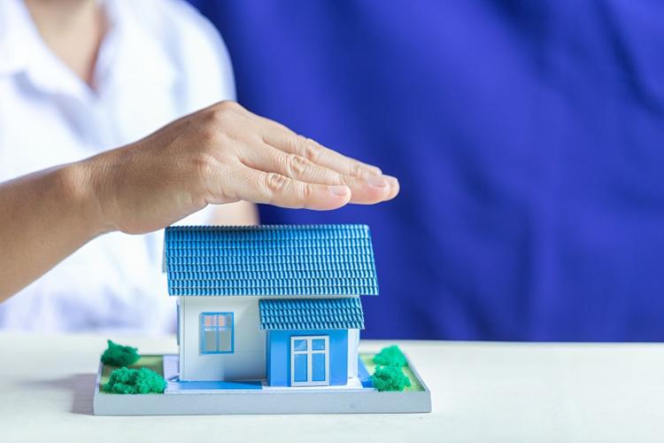 A man placing his hand over a model house to indicate protection