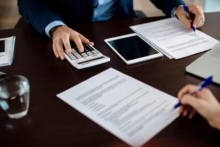 Two people are signing documents, facing each other, while one of them is using a calculator