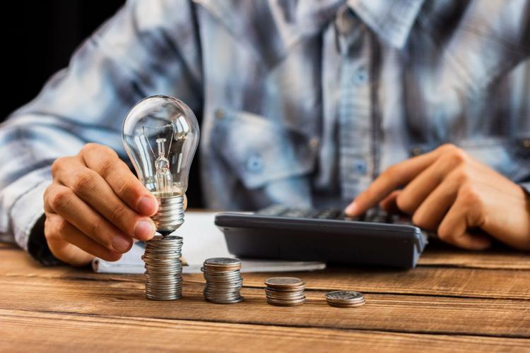 A man using a calculator to count while placing a bulb on a stack of coins