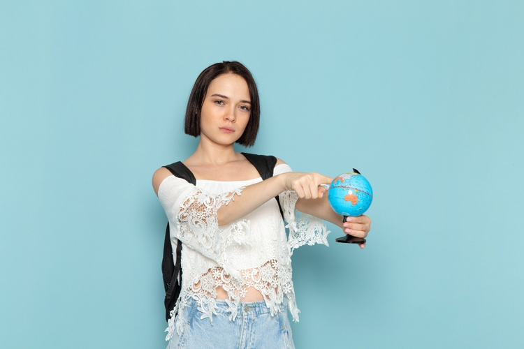 A young Asian woman with a black backpack and a white lace top points at a small globe