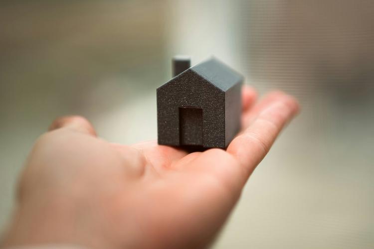 A hand holding a black model house in its palm