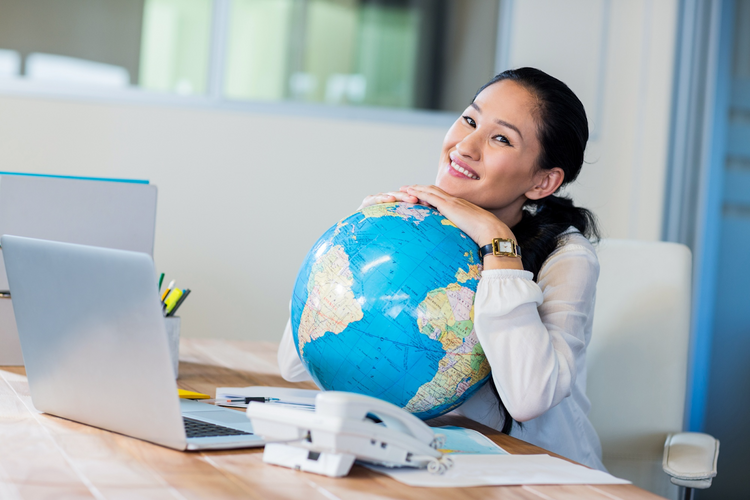 A smiling woman sitting at a desk, embracing a large blue globe