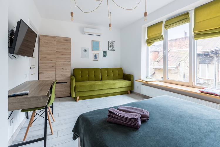 A bright, modern studio apartment features a green sofa, a light wood desk and a closet