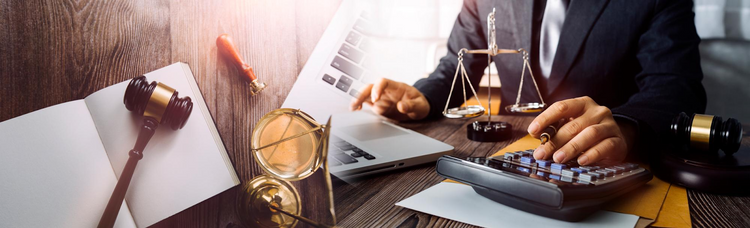A person in a suit works on a laptop and a calculator on a desk with legal items