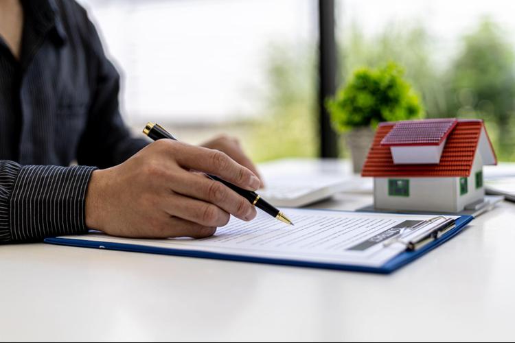 A man signing an agreement on the table, and a model house is placed beside him.