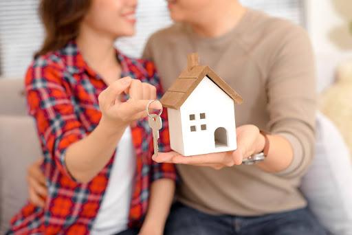 Happy couple holding house model and new home keys.