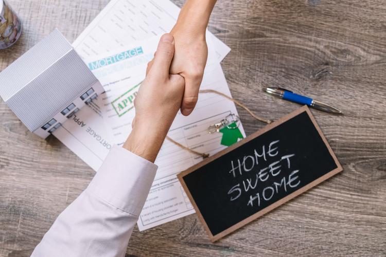 Handshake over approved home loan documents and a sign reading home sweet home.