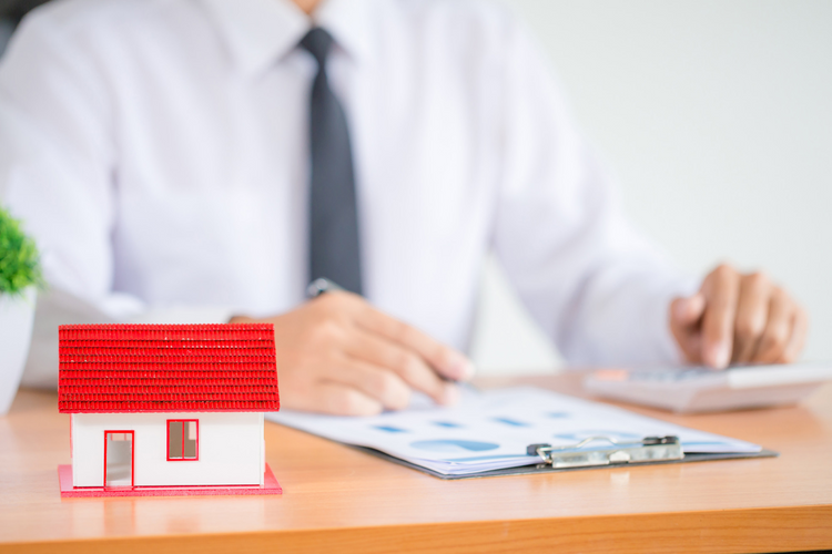 Real estate agent reviewing documents beside a small house model.