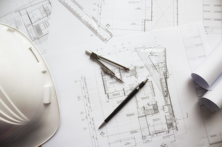 Architectural blueprints with a white hard hat, ruler, compass, and pen.