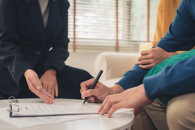 Close-up of an insurer guiding a couple on where to sign a document.