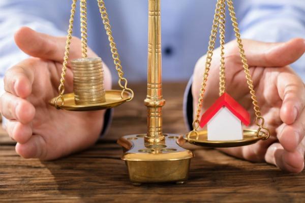 Man balancing a toy house and coins on a scale