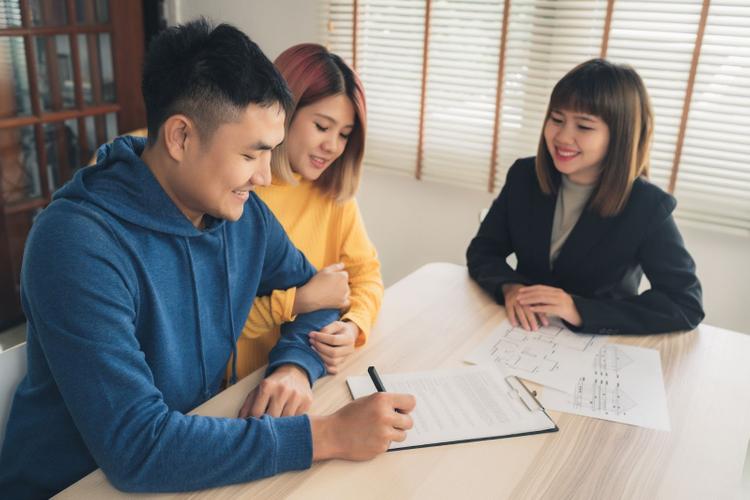 Malaysian couple finalising paperwork with an agent in an office setting.
